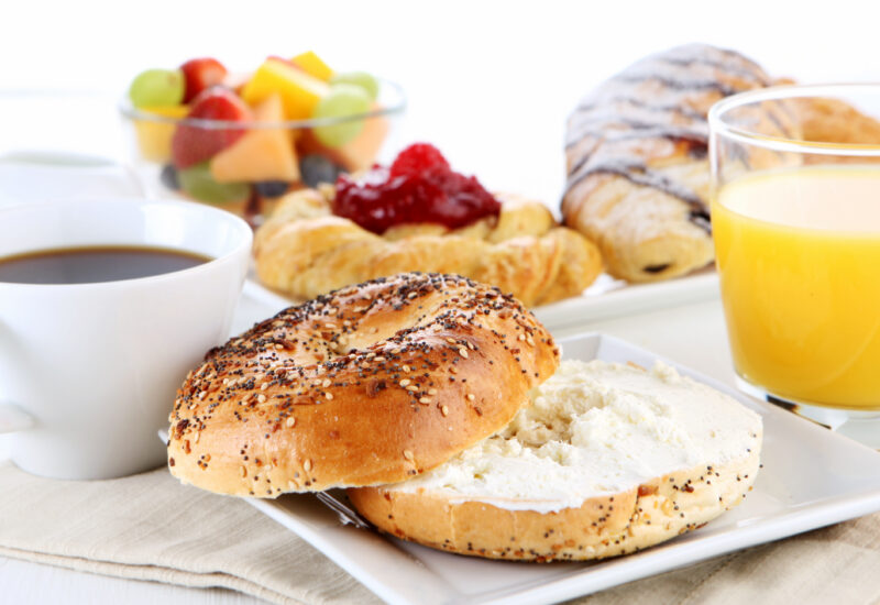 Breakfast spread with a bagel and cream cheese, pastries, fresh fruit, coffee and orange juice.