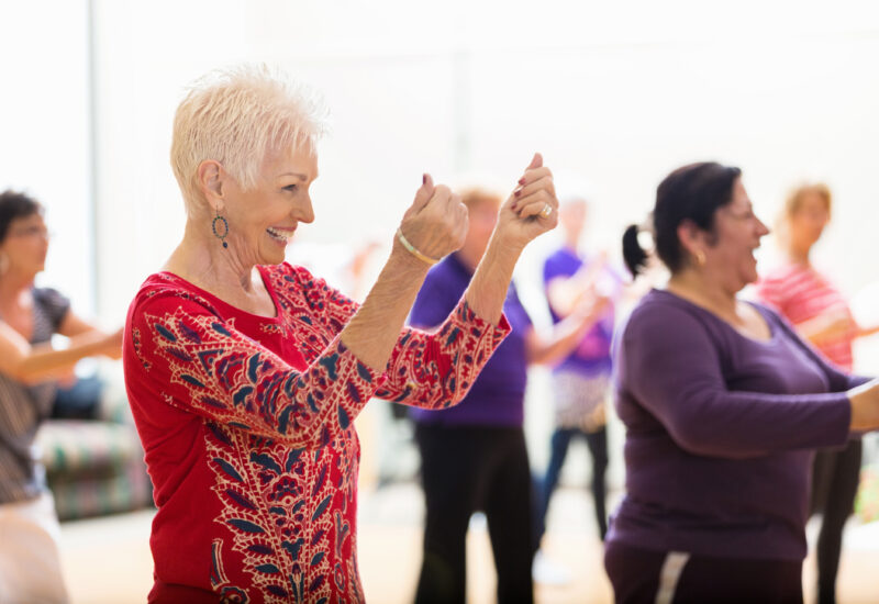 Older adults smiling and dancing together during a lively group activity.